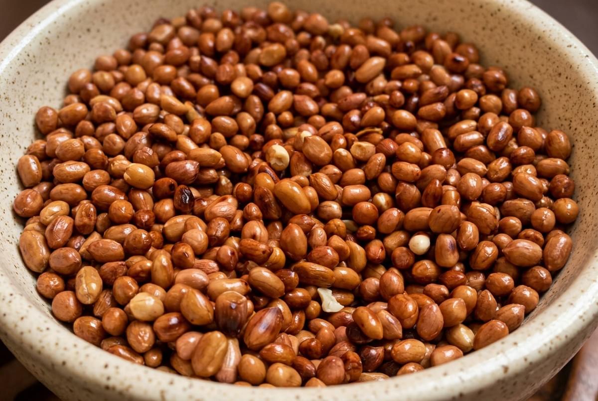 Close-up of roasted, skin-on peanuts filling a beige ceramic bowl. Close-up of roasted, skin-on peanuts filling a beige ceramic bowl.