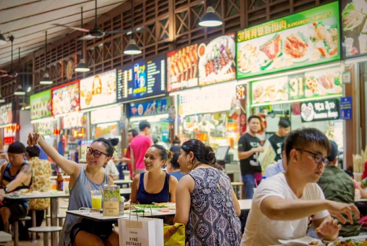 Friends smiling and taking a selfie while dining at a brightly lit hawker center. Friends smiling and taking a selfie while dining at a brightly lit hawker center.