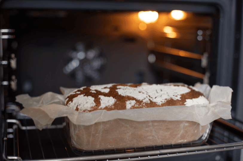 A rustic loaf of artisan bread with a beautifully floured, cracked crust baking in a glass loaf pan inside a hot oven, showing how sustained high baking temperatures create essential oven spring and deep crust development in yeast breads. A rustic loaf of artisan bread with a beautifully floured, cracked crust baking in a glass loaf pan inside a hot oven, showing how sustained high baking temperatures create essential oven spring and deep crust development in yeast breads.