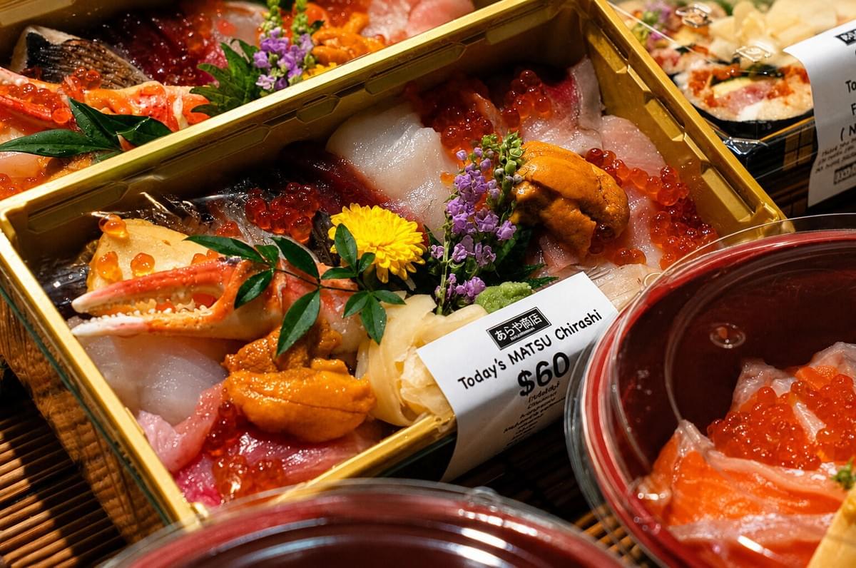 Array of packaged sushi sets and sashimi bowls on a bamboo mat display. Array of packaged sushi sets and sashimi bowls on a bamboo mat display.