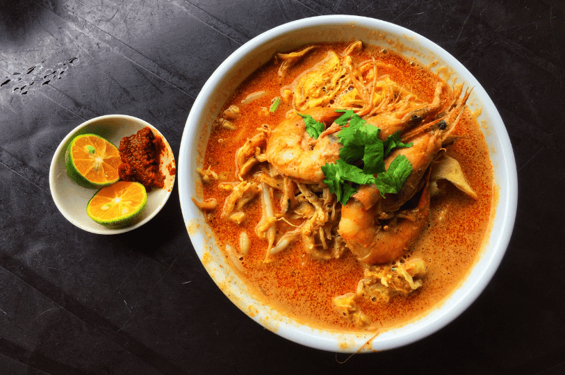 A top-down view of a hearty bowl of laksa topped with large whole prawns, shredded chicken, bean sprouts, and fresh cilantro, served next to a small dish of calamansi lime halves and sambal.Blanched broccoli inside a mesh strainer being submerged into a glass bowl of ice water to immediately stop the cooking process. A top-down view of a hearty bowl of laksa topped with large whole prawns, shredded chicken, bean sprouts, and fresh cilantro, served next to a small dish of calamansi lime halves and sambal.Blanched broccoli inside a mesh strainer being submerged into a glass bowl of ice water to immediately stop the cooking process.