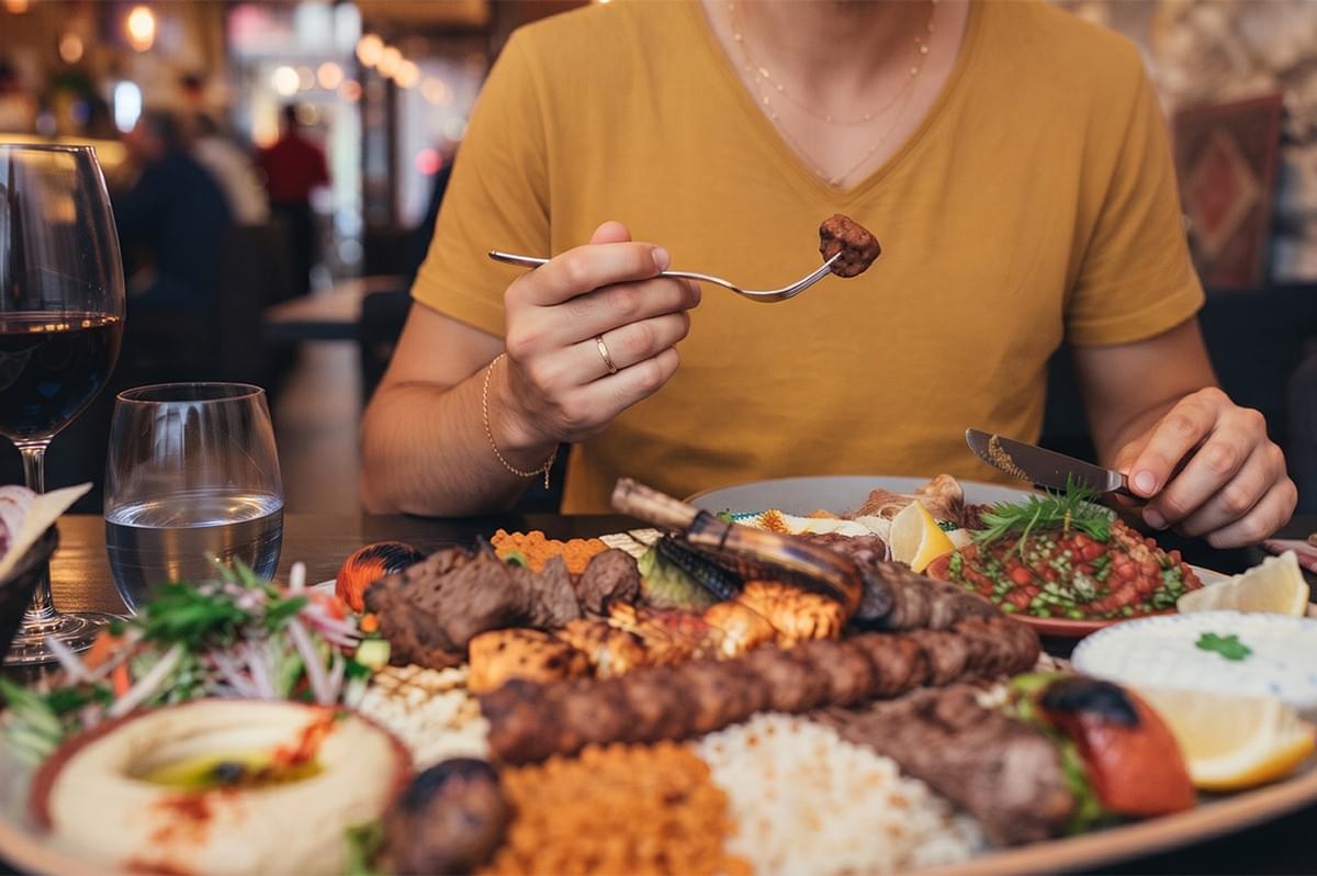 Person eating a traditional Turkish mixed kebab platter with hummus and salad at a restaurant. Person eating a traditional Turkish mixed kebab platter with hummus and salad at a restaurant.