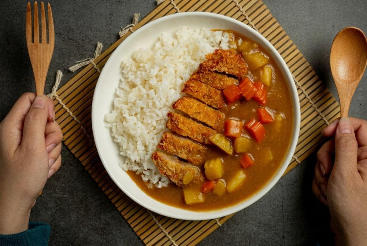 Top-down view of a plate of Japanese chicken katsu curry with rice, held with a wooden fork and spoon. Top-down view of a plate of Japanese chicken katsu curry with rice, held with a wooden fork and spoon.