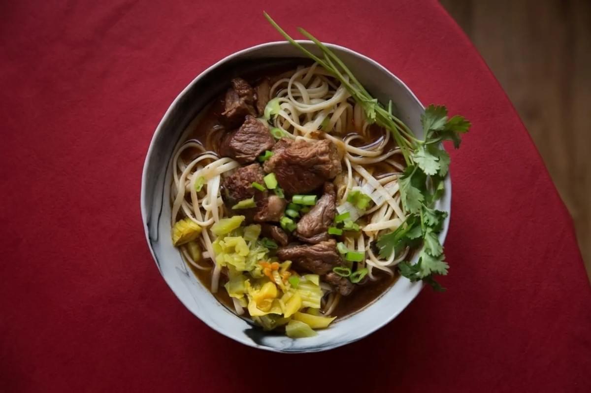 Top-down view of Taiwanese beef noodle soup with braised beef, noodles, and cilantro on a red tablecloth Top-down view of Taiwanese beef noodle soup with braised beef, noodles, and cilantro on a red tablecloth