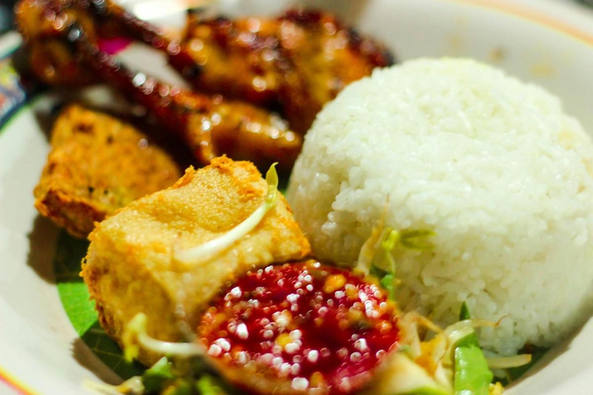 A plate of Indonesian food features a dome of white rice, grilled chicken, a piece of fried tofu, and a side of fresh bean sprouts. In the foreground, a vibrant red sambal chili paste serves as a focal point for the dish. A plate of Indonesian food features a dome of white rice, grilled chicken, a piece of fried tofu, and a side of fresh bean sprouts. In the foreground, a vibrant red sambal chili paste serves as a focal point for the dish.