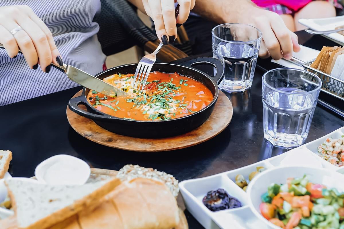 Close-up eye-level angle of Israeli shakshuka in a cast iron skillet, eggs poached in rich tomato sauce with herbs, served with bread and salad as a comfort food meal Close-up eye-level angle of Israeli shakshuka in a cast iron skillet, eggs poached in rich tomato sauce with herbs, served with bread and salad as a comfort food meal