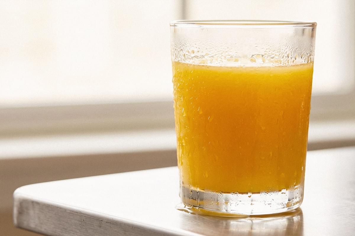 A glass of orange juice on a white surface, with condensation visible on the glass. A glass of orange juice on a white surface, with condensation visible on the glass.