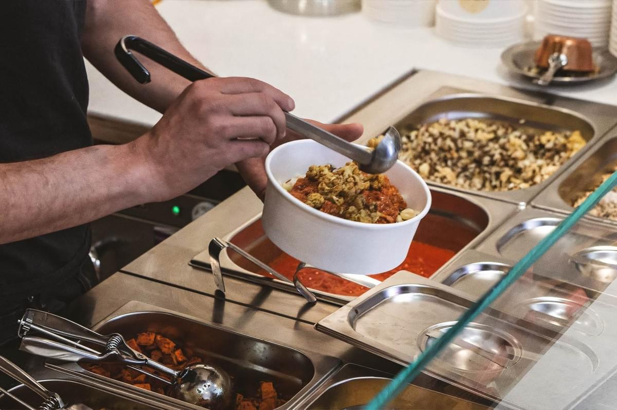 Food counter scene where a fresh bowl of Egyptian koshari is being assembled with tomato sauce, lentils, pasta, and chickpeas. Food counter scene where a fresh bowl of Egyptian koshari is being assembled with tomato sauce, lentils, pasta, and chickpeas.