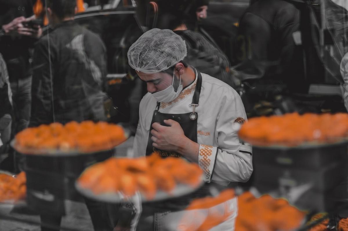 Chef wearing a face mask and hairnet preparing traditional Turkish baklava in a professional kitchen. Chef wearing a face mask and hairnet preparing traditional Turkish baklava in a professional kitchen.