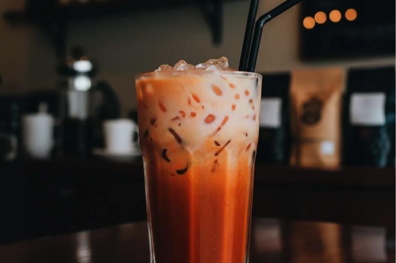 A tall glass of Gula Melaka Kopi with two black straws, showing layers of milk mixing with dark coffee. A tall glass of Gula Melaka Kopi with two black straws, showing layers of milk mixing with dark coffee.