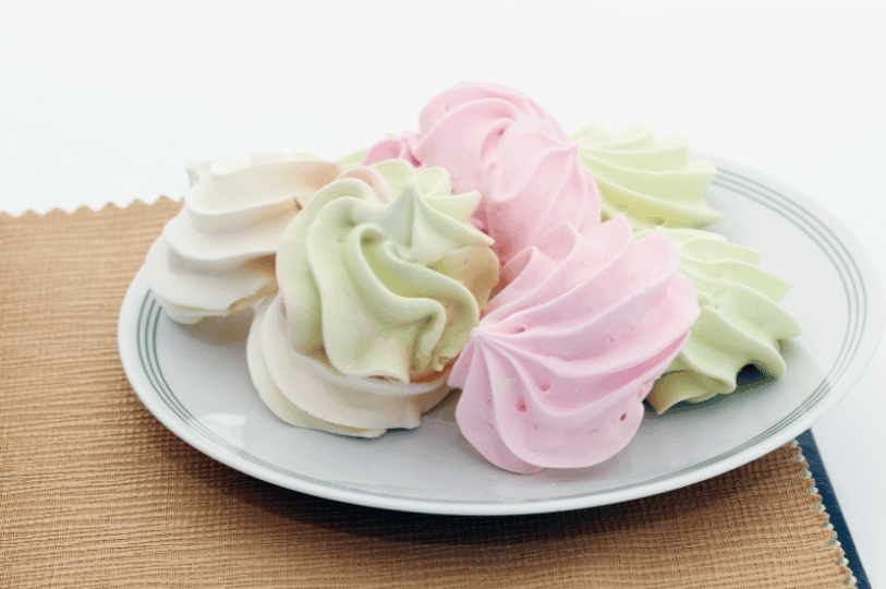 A plate of colorful pastel meringue cookies in shades of soft pink, mint green, and off-white, served on a white plate with a brown textured placemat. A plate of colorful pastel meringue cookies in shades of soft pink, mint green, and off-white, served on a white plate with a brown textured placemat.