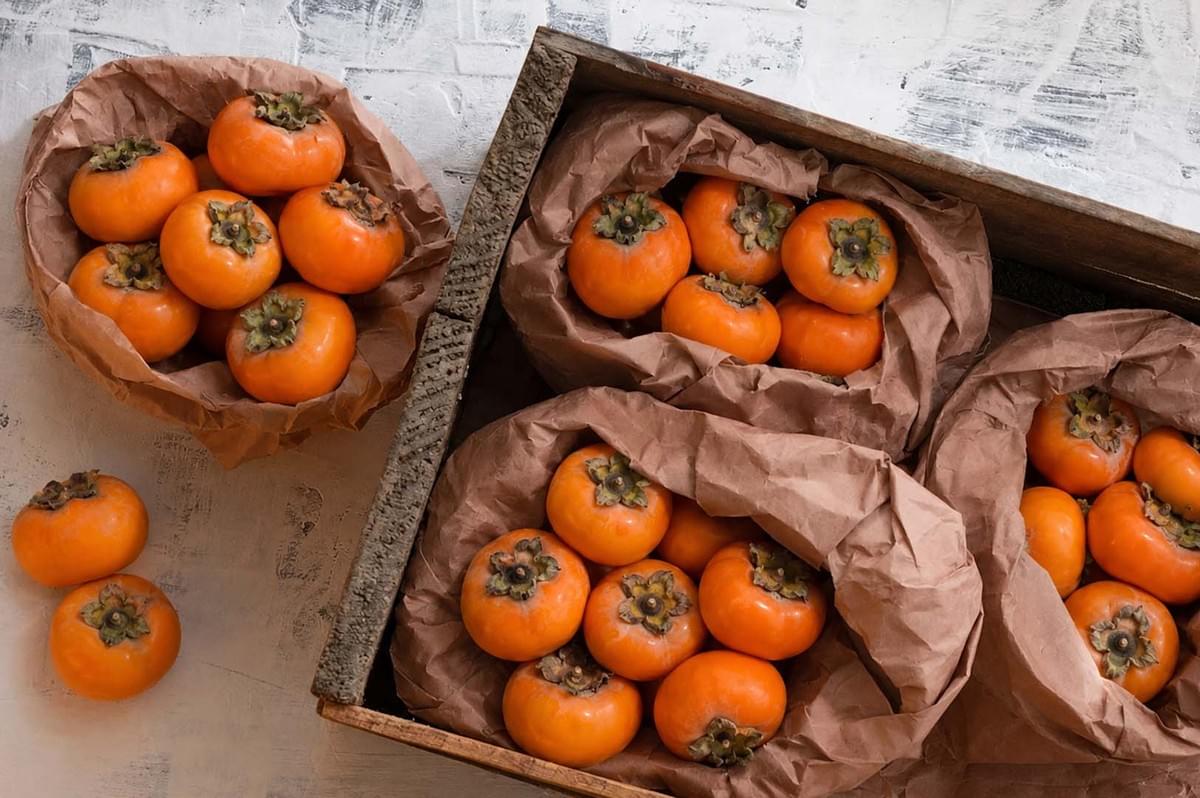 Fresh persimmons arranged in paper bags and wooden crate Fresh persimmons arranged in paper bags and wooden crate
