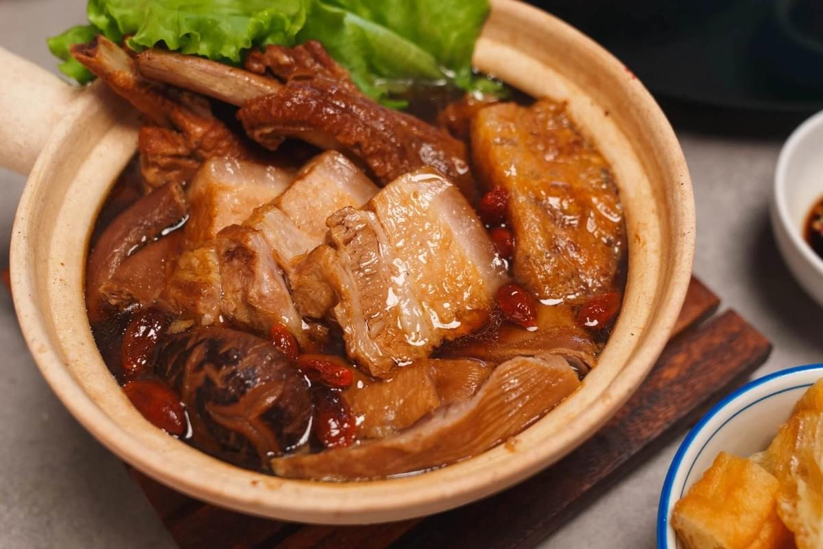 This image features a traditional Malaysian Bak Kut Teh, a hearty herbal soup filled with tender pork ribs and pork belly. The dish is served in a classic clay pot, garnished with fresh lettuce and accompanied by a side of fried dough crullers. This image features a traditional Malaysian Bak Kut Teh, a hearty herbal soup filled with tender pork ribs and pork belly. The dish is served in a classic clay pot, garnished with fresh lettuce and accompanied by a side of fried dough crullers.
