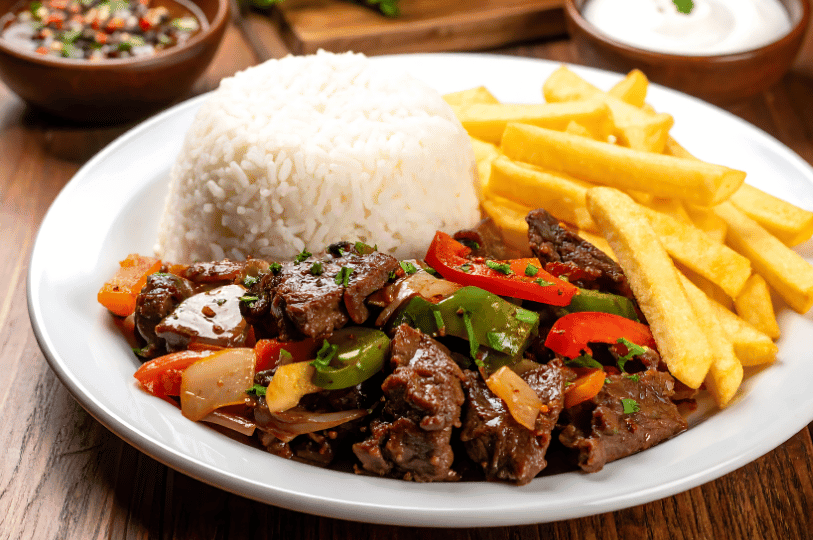 A brightly lit plate of Lomo Saltado featuring a large mound of white rice, a side of golden-brown french fries, and the signature beef stir-fry with green and red peppers in a savory sauce. A brightly lit plate of Lomo Saltado featuring a large mound of white rice, a side of golden-brown french fries, and the signature beef stir-fry with green and red peppers in a savory sauce.