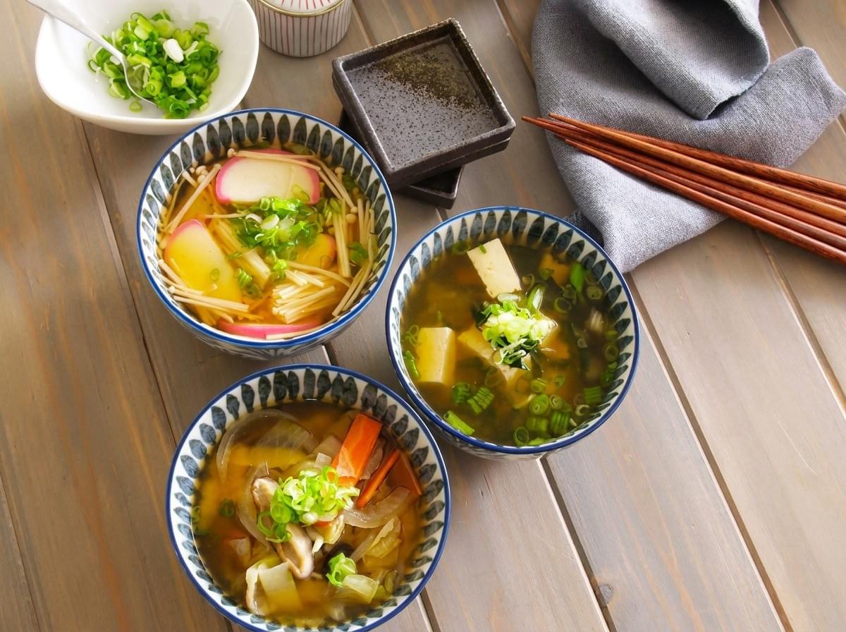 Three bowls of Japanese soups with various toppings arranged on a wooden table. Three bowls of Japanese soups with various toppings arranged on a wooden table.