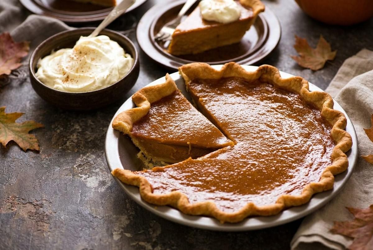 Pumpkin pie in a baking dish with a slice cut out next to a bowl of whipped cream. Pumpkin pie in a baking dish with a slice cut out next to a bowl of whipped cream.