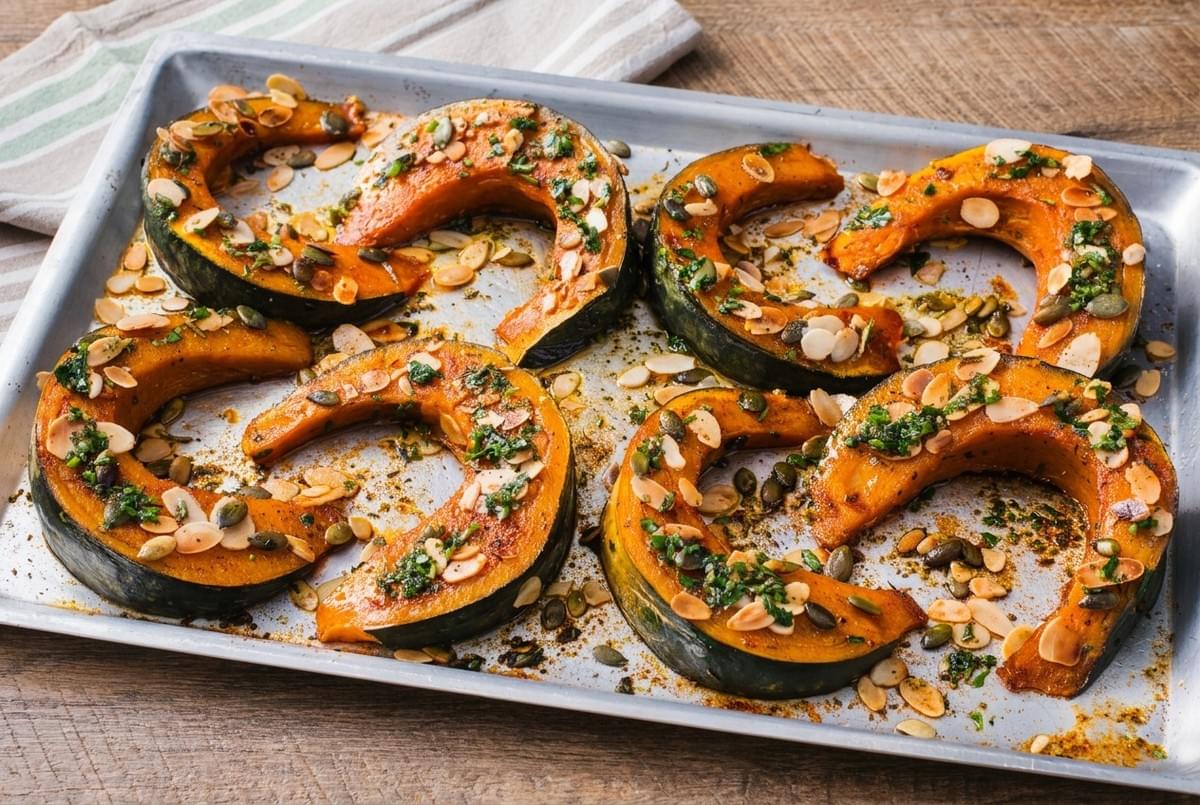 Sheet pan of roasted pumpkin wedges topped with flaked almonds, pumpkin seeds, and fresh herbs. Sheet pan of roasted pumpkin wedges topped with flaked almonds, pumpkin seeds, and fresh herbs.