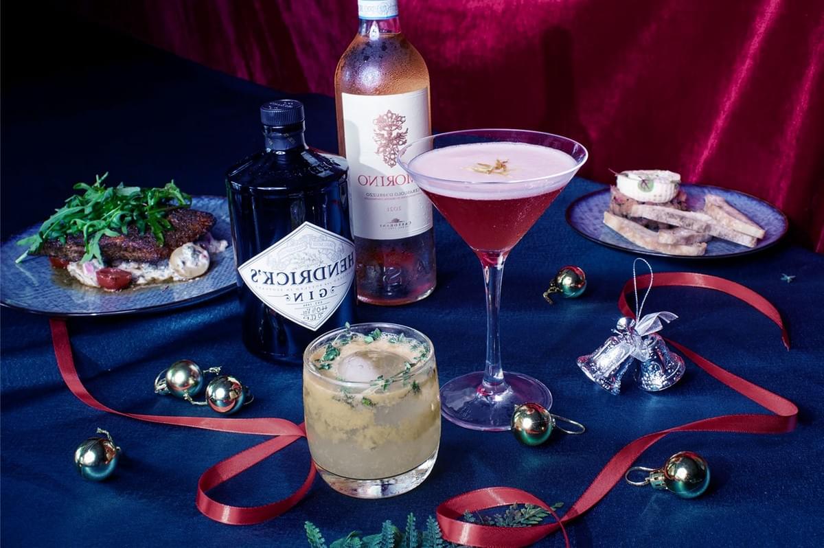 Festive table with cocktails, a bottle of gin, and wine. Plates of steak and bruschetta alongside holiday decorations convey a celebratory mood. Festive table with cocktails, a bottle of gin, and wine. Plates of steak and bruschetta alongside holiday decorations convey a celebratory mood.