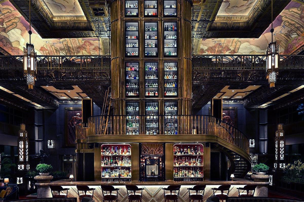 Luxurious bar interior with a tall, ornate liquor shelf, spiral staircase, and art deco design. Warm lighting and intricate ceiling details create an opulent atmosphere. Luxurious bar interior with a tall, ornate liquor shelf, spiral staircase, and art deco design. Warm lighting and intricate ceiling details create an opulent atmosphere.