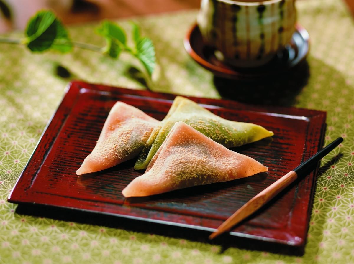 Triangular yatsuhashi mochi sweets served on a dark wooden lacquer tray next to a tea set. Triangular yatsuhashi mochi sweets served on a dark wooden lacquer tray next to a tea set.