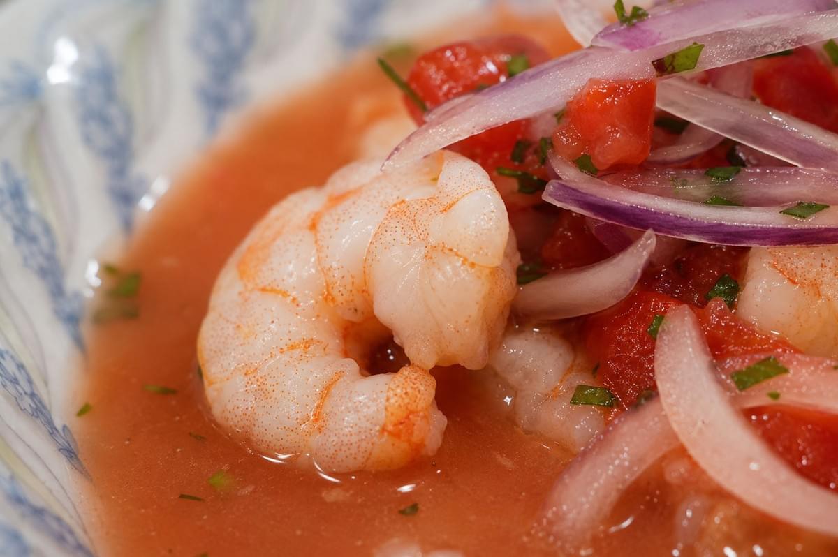Close-up of a cooked shrimp in tangy tomato-based ceviche sauce topped with red onion slices and herbs Close-up of a cooked shrimp in tangy tomato-based ceviche sauce topped with red onion slices and herbs
