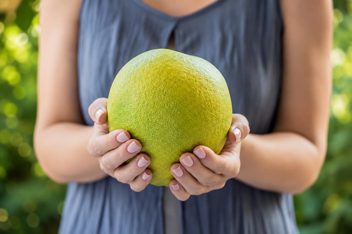 A person holding a large, green pomelo fruit with both hands. A person holding a large, green pomelo fruit with both hands.