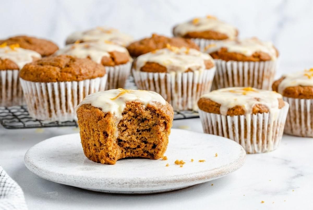 Pumpkin spice muffin with a bite taken out, showing iced glaze on a white plate. Pumpkin spice muffin with a bite taken out, showing iced glaze on a white plate.