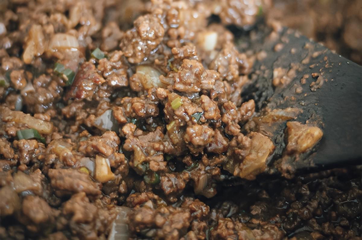 Extreme close-up, overhead angle of spiced ground beef filling cooking for Jamaican patties with onions, herbs, and seasoned sauce. Extreme close-up, overhead angle of spiced ground beef filling cooking for Jamaican patties with onions, herbs, and seasoned sauce.