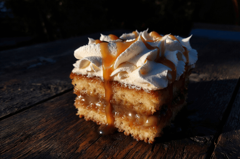 A square slice of Tres Leches cake sitting on a rustic wooden surface, topped with peaks of whipped cream and a generous drizzle of golden caramel sauce dripping down the sides. A square slice of Tres Leches cake sitting on a rustic wooden surface, topped with peaks of whipped cream and a generous drizzle of golden caramel sauce dripping down the sides.