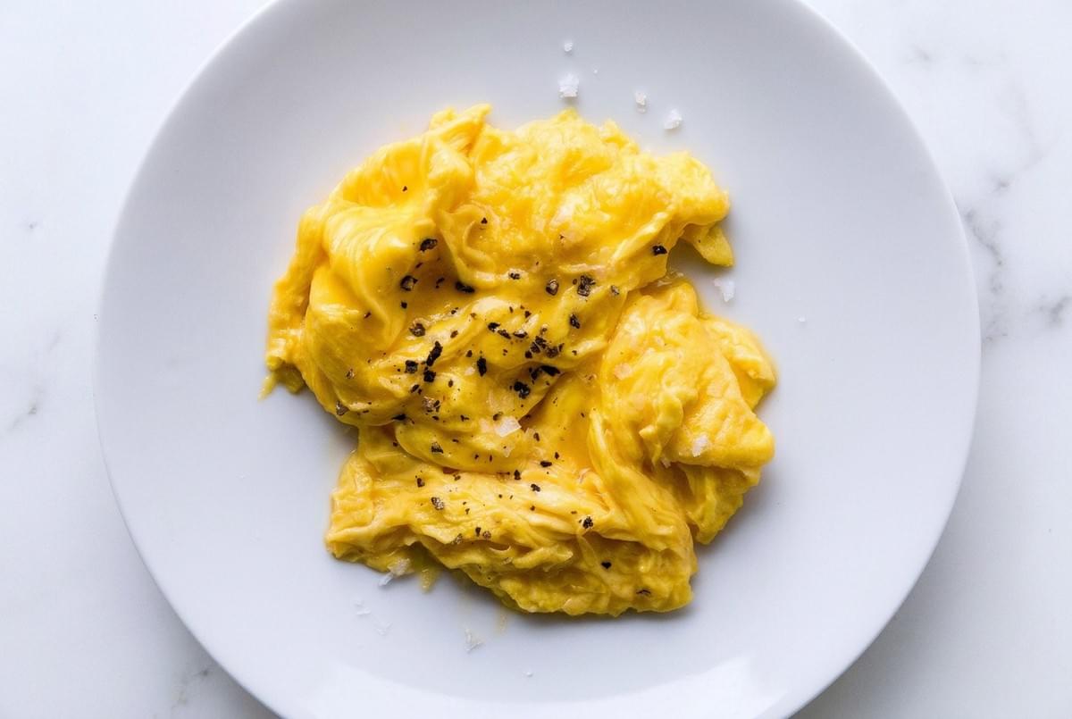 Soft scrambled eggs seasoned with cracked black pepper and flaky sea salt on a white plate. Soft scrambled eggs seasoned with cracked black pepper and flaky sea salt on a white plate.