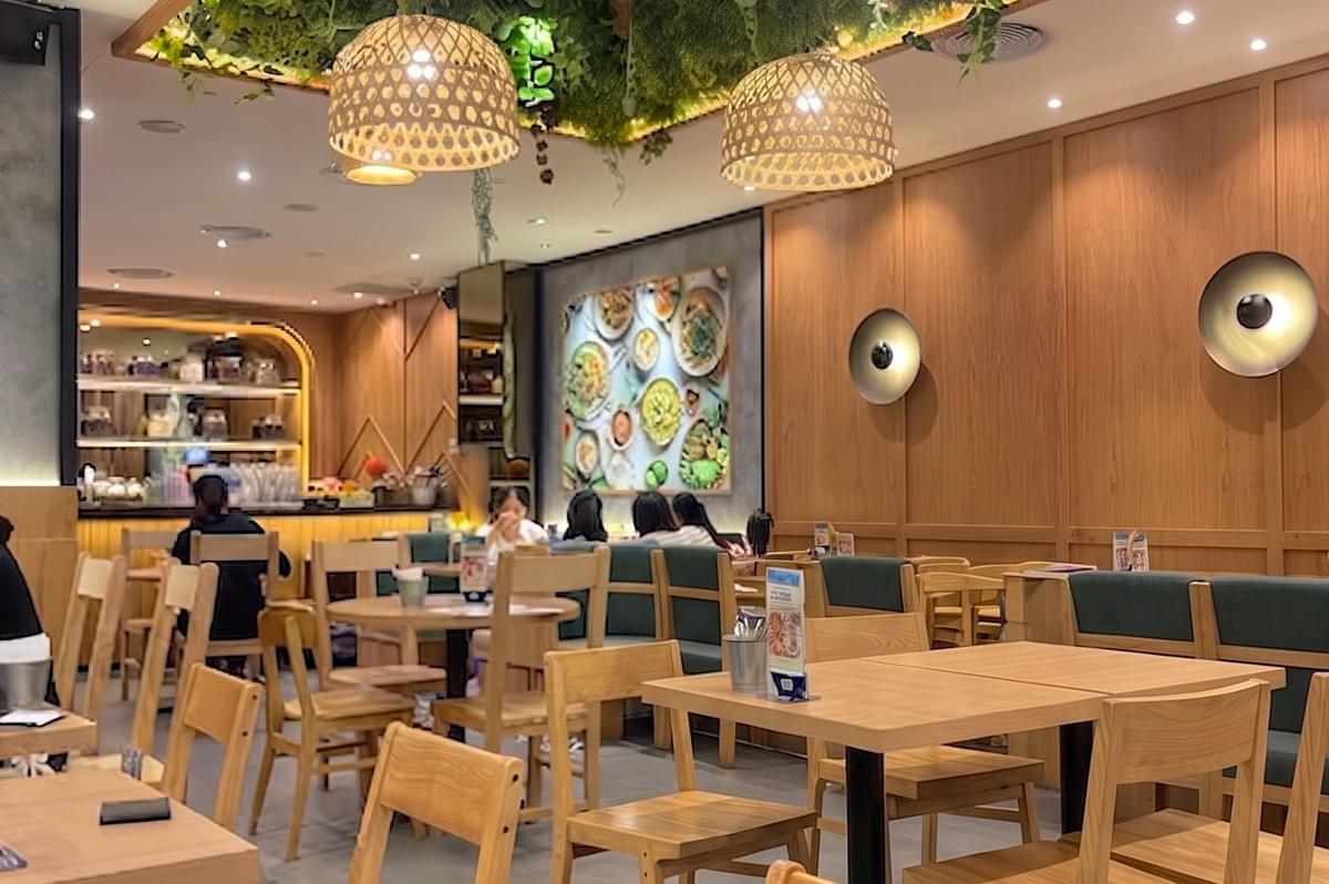 Interior view of Sanook Kitchen Halal restaurant featuring wooden tables and a green leaf ceiling decor. Interior view of Sanook Kitchen Halal restaurant featuring wooden tables and a green leaf ceiling decor.