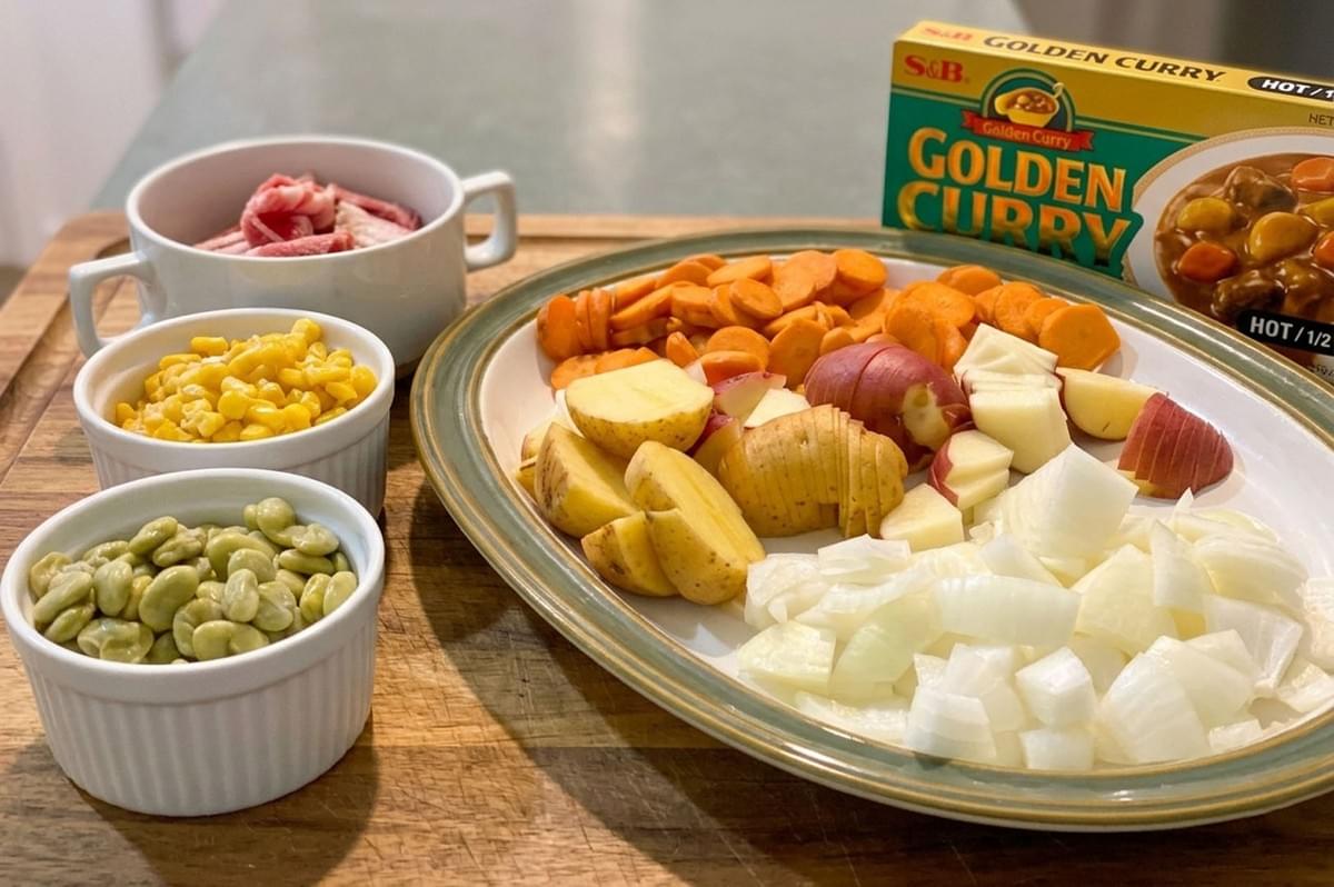Array of chopped ingredients including potatoes, carrots, onions, and meat next to a box of S&B Golden Curry roux Array of chopped ingredients including potatoes, carrots, onions, and meat next to a box of S&B Golden Curry roux