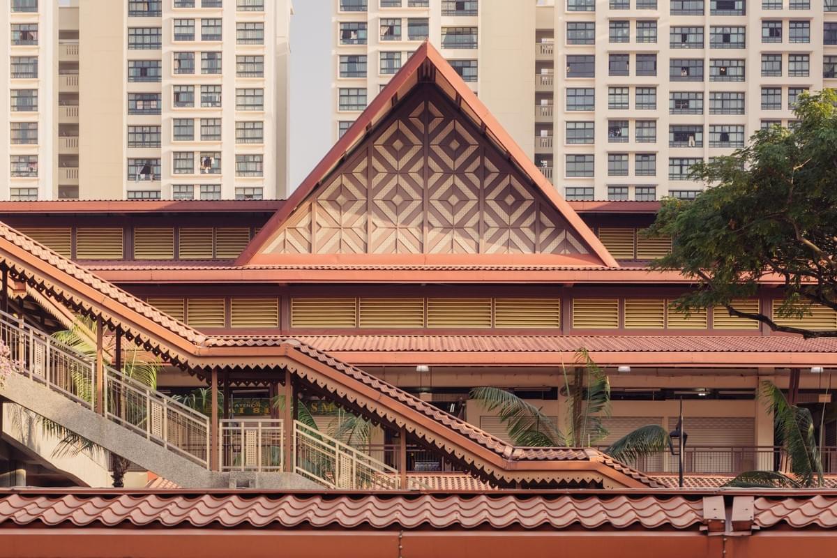 This image showcases the Geylang Serai Market, featuring its distinctive Malay-inspired tiered roof with intricate geometric patterns. Modern high-rise apartment buildings stand directly behind the traditional architecture, illustrating the contrast between heritage and urban development in Singapore. This image showcases the Geylang Serai Market, featuring its distinctive Malay-inspired tiered roof with intricate geometric patterns. Modern high-rise apartment buildings stand directly behind the traditional architecture, illustrating the contrast between heritage and urban development in Singapore.
