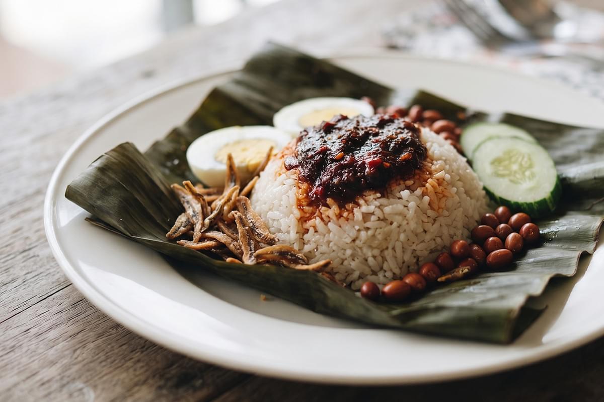 Nasi Lemak served on a banana leaf with rice, sambal, anchovies, peanuts, cucumber, and hard-boiled egg. Nasi Lemak served on a banana leaf with rice, sambal, anchovies, peanuts, cucumber, and hard-boiled egg.