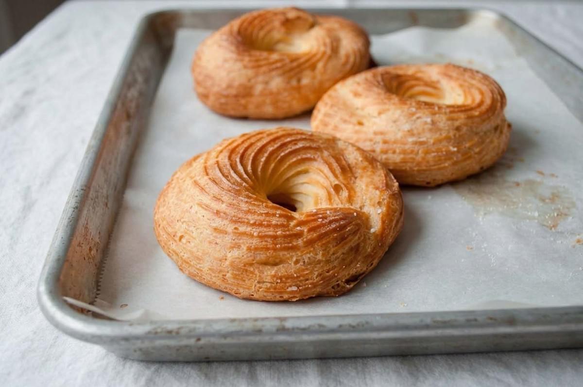 Three golden-brown baked choux pastry rings arranged on a parchment-lined baking sheet Three golden-brown baked choux pastry rings arranged on a parchment-lined baking sheet