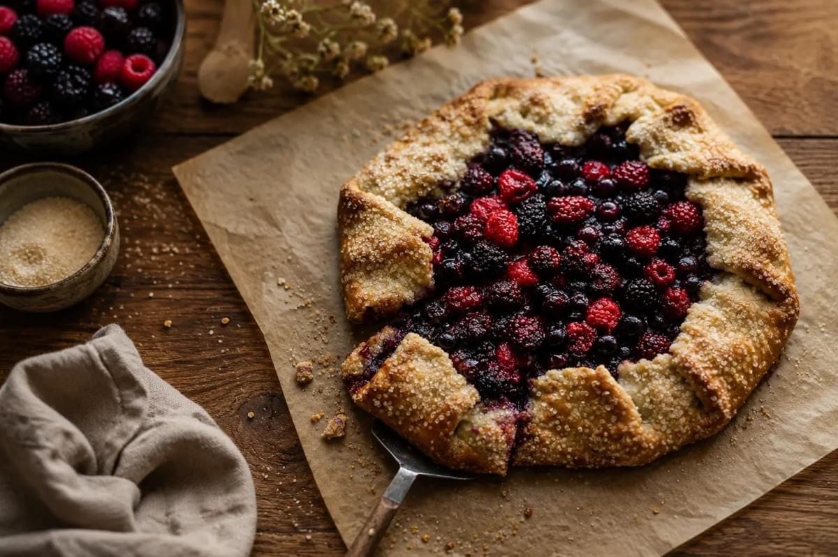 A rustic mixed berry galette on parchment paper, sprinkled with coarse sugar. A rustic mixed berry galette on parchment paper, sprinkled with coarse sugar.