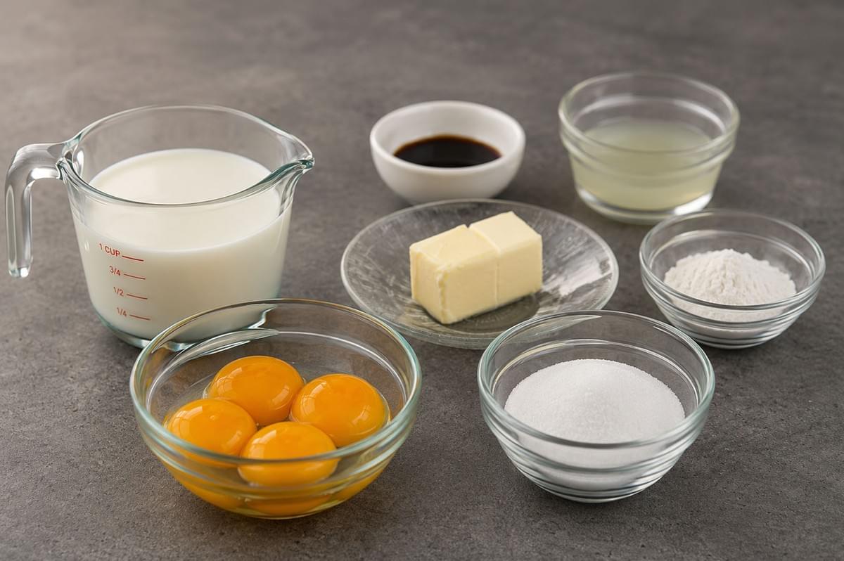 Ingredients for pastry cream including milk, egg yolks, sugar, butter, flour, and vanilla arranged in glass bowls on a grey surface Ingredients for pastry cream including milk, egg yolks, sugar, butter, flour, and vanilla arranged in glass bowls on a grey surface