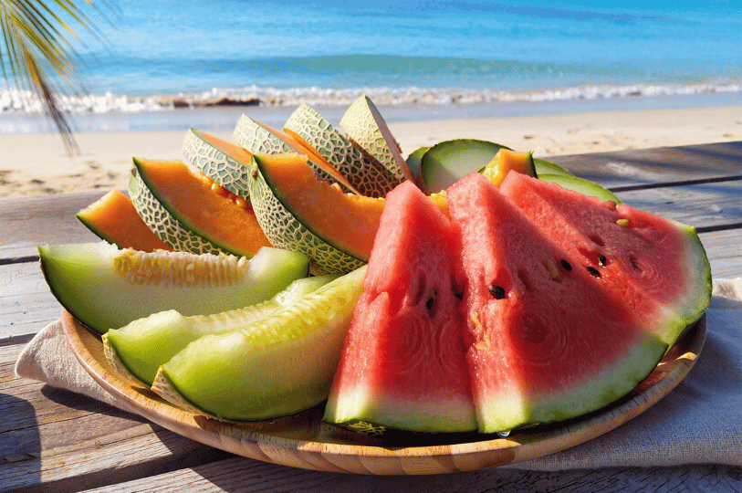 A refreshing platter of sliced watermelon, cantaloupe, and honeydew melon served on a wooden plate on a sun-drenched beach with the ocean in the background. A refreshing platter of sliced watermelon, cantaloupe, and honeydew melon served on a wooden plate on a sun-drenched beach with the ocean in the background.
