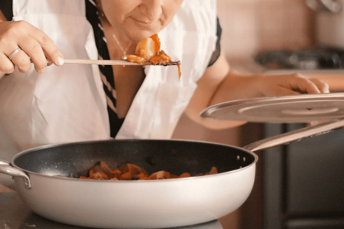 Elderly woman tasting cooked food on the pan Elderly woman tasting cooked food on the pan