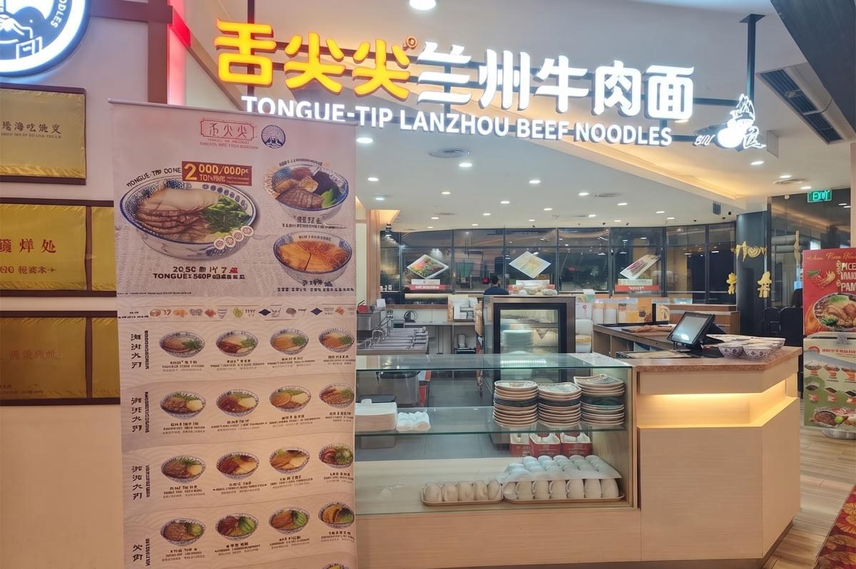 Storefront of Tongue-Tip Lanzhou Beef Noodles restaurant featuring a menu banner and counter. Storefront of Tongue-Tip Lanzhou Beef Noodles restaurant featuring a menu banner and counter.