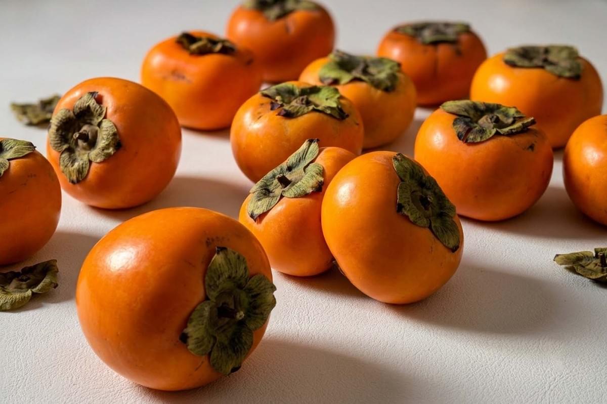Fresh orange persimmons arranged on white surface Fresh orange persimmons arranged on white surface