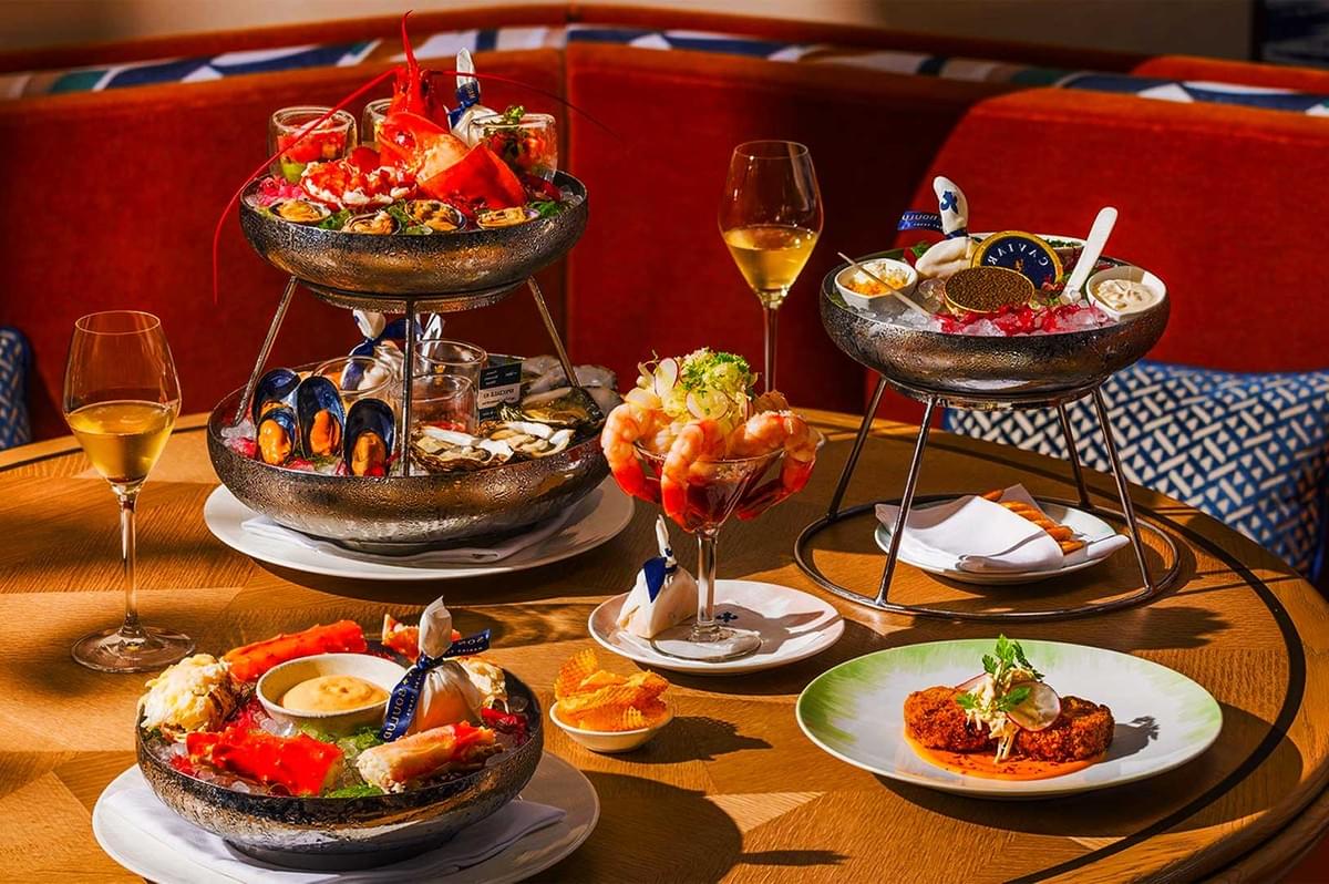 A sophisticated seafood spread on a round table, featuring lobster, mussels, shrimp cocktail, and caviar, complemented by two glasses of white wine. A sophisticated seafood spread on a round table, featuring lobster, mussels, shrimp cocktail, and caviar, complemented by two glasses of white wine.