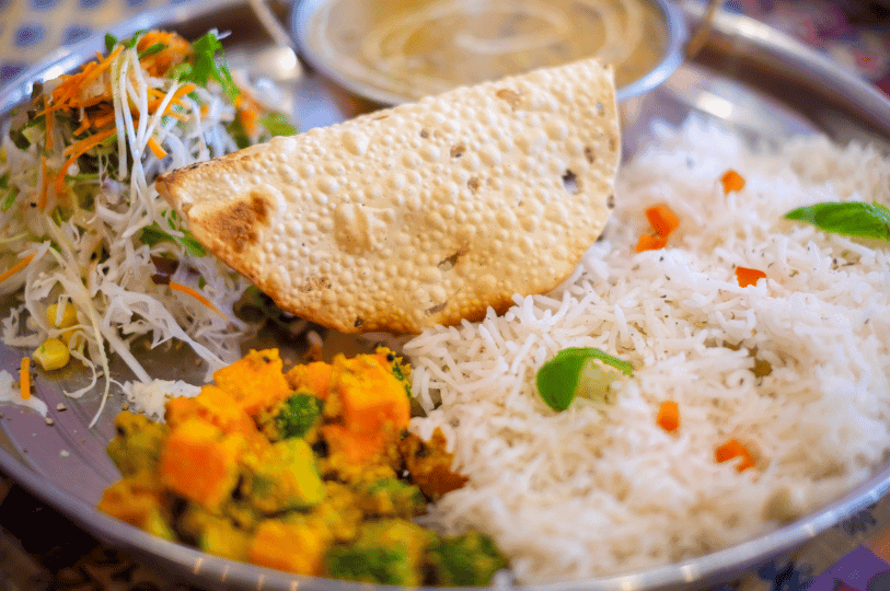 A bright, overhead shot of a Dal Bhat platter showcasing fluffy white rice, a large folded papadum, a vegetable stir-fry, and a side of finely shredded fresh salad. A bright, overhead shot of a Dal Bhat platter showcasing fluffy white rice, a large folded papadum, a vegetable stir-fry, and a side of finely shredded fresh salad.