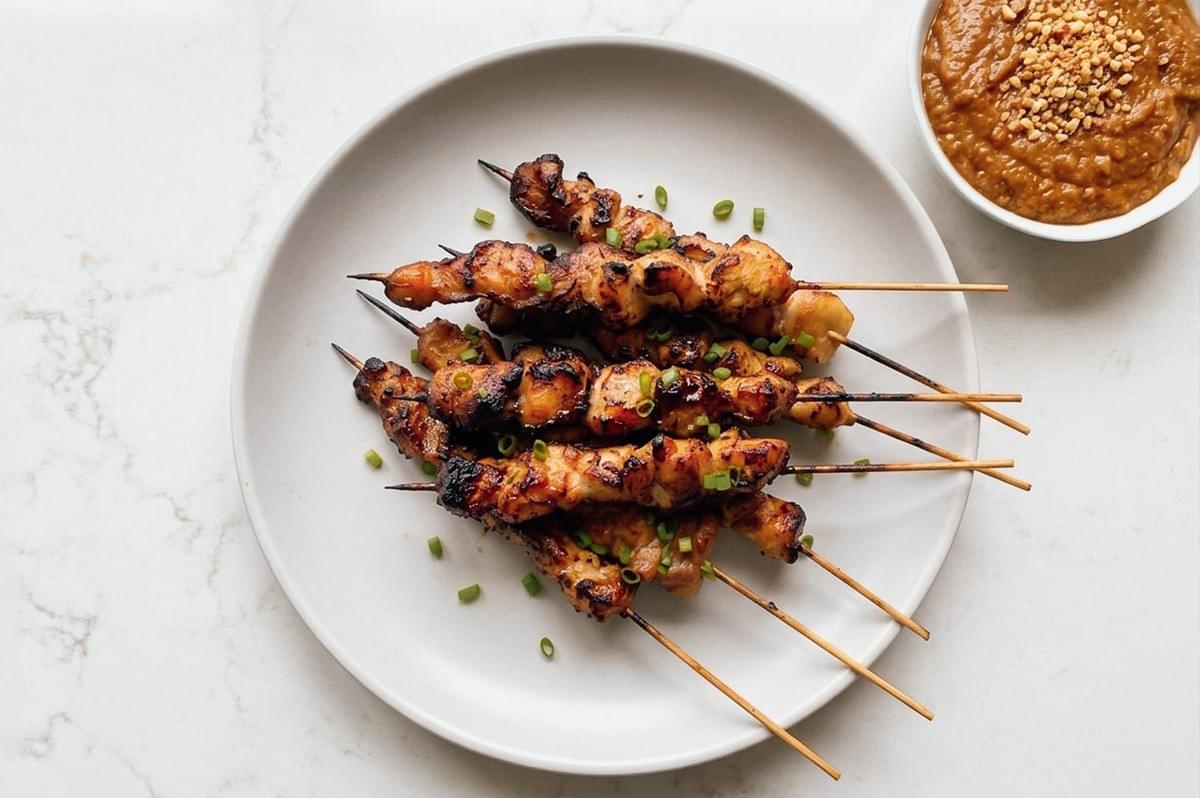 Top-down flat lay shot of grilled chicken satay skewers on a plate with peanut sauce and chopped green onions, showcasing Indonesian street food style Top-down flat lay shot of grilled chicken satay skewers on a plate with peanut sauce and chopped green onions, showcasing Indonesian street food style