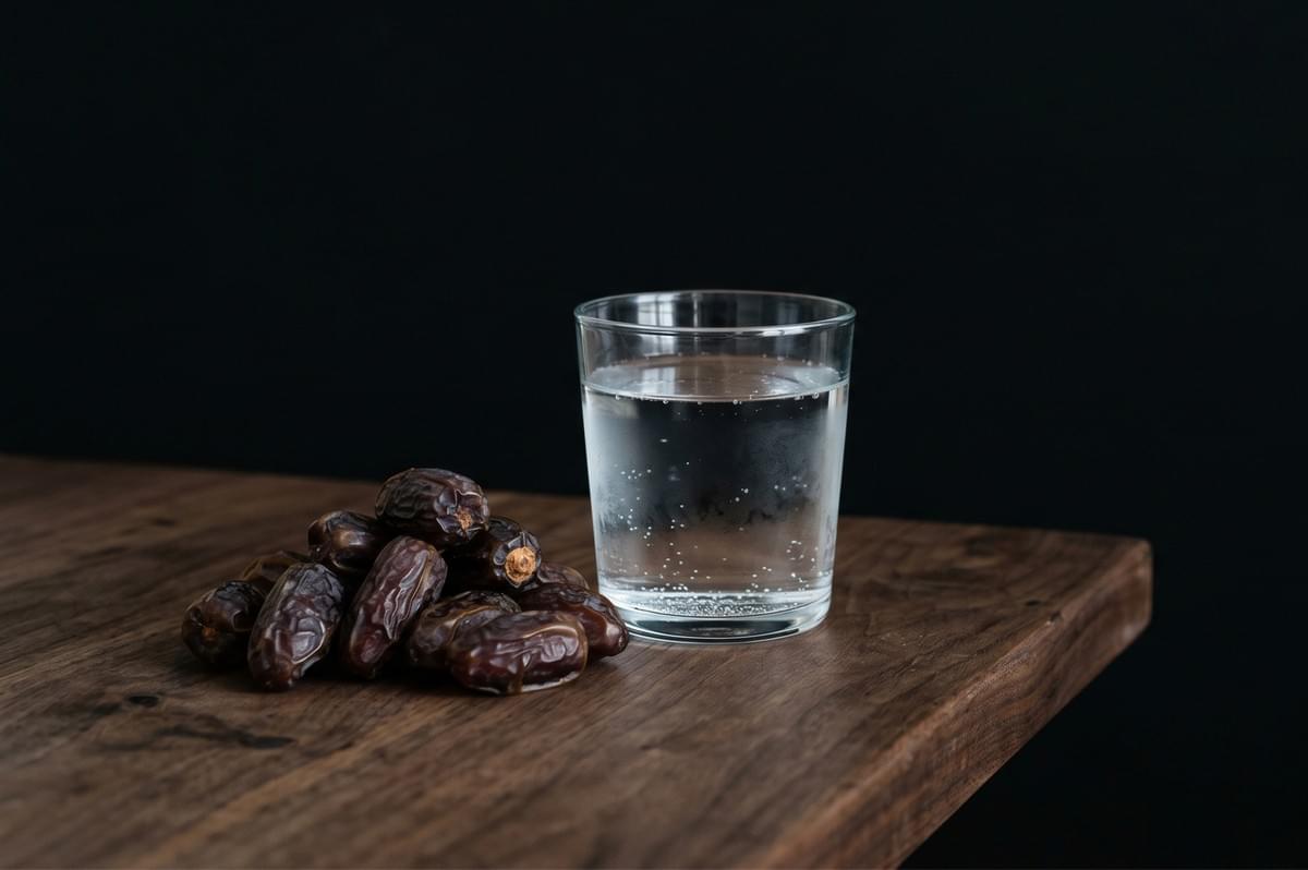 A glass of water next to a pile of dried dates on a wooden table. A glass of water next to a pile of dried dates on a wooden table.