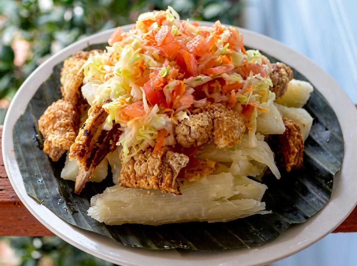 Served traditionally on a deep green banana leaf, this brightly lit street-food feast pairs golden, crispy chicharrones with starchy white yucca and a vivid tomato-and-cabbage curtido for an incredibly fresh, authentic tropical vibe. Served traditionally on a deep green banana leaf, this brightly lit street-food feast pairs golden, crispy chicharrones with starchy white yucca and a vivid tomato-and-cabbage curtido for an incredibly fresh, authentic tropical vibe.