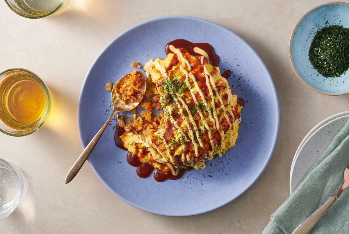 Top-down view of omurice on a blue plate drizzled with mayonnaise and dark sauce, served w Top-down view of omurice on a blue plate drizzled with mayonnaise and dark sauce, served w