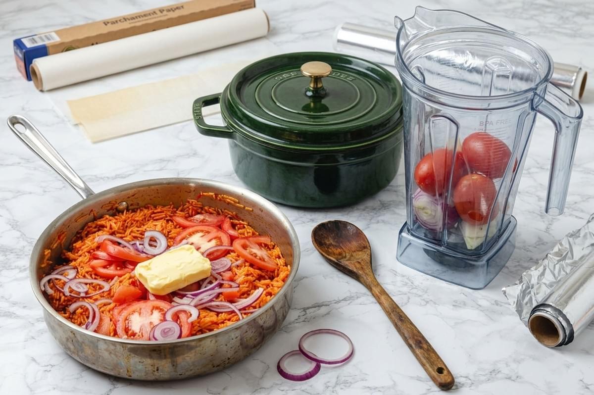 Kitchen counter with a pan of rice topped with tomatoes, onions, and butter next to a blender with ingredients Kitchen counter with a pan of rice topped with tomatoes, onions, and butter next to a blender with ingredients