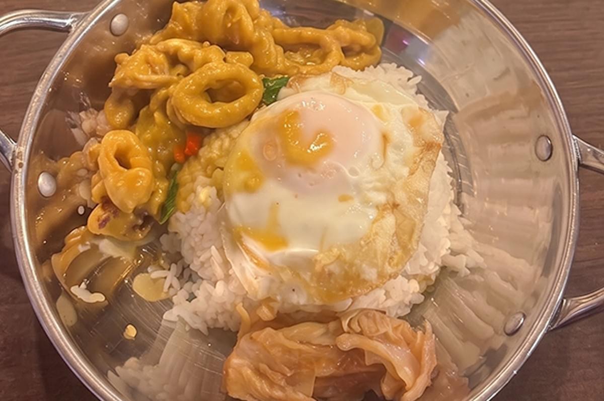 Salted egg sotong rice bowl topped with a fried egg in a metal dish. Salted egg sotong rice bowl topped with a fried egg in a metal dish.