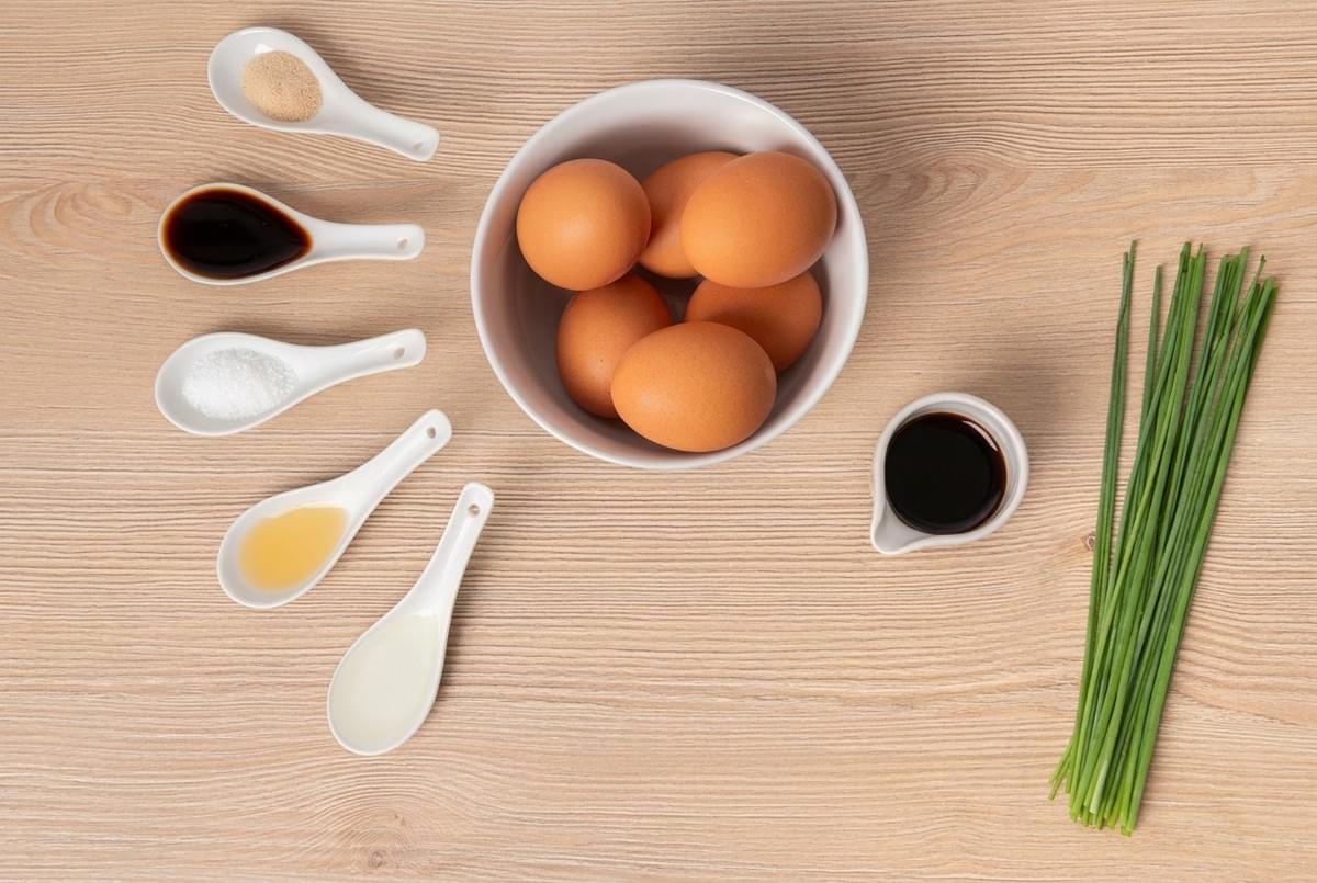 Ingredients for tamagoyaki flat lay, including brown eggs, soy sauce, liquid seasonings, and fresh chives. Ingredients for tamagoyaki flat lay, including brown eggs, soy sauce, liquid seasonings, and fresh chives.